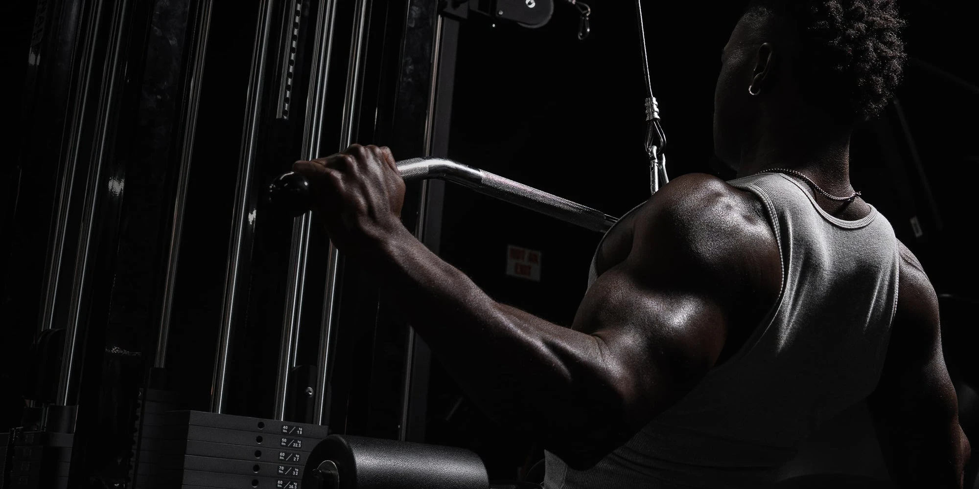 Athlete in a ribbed tank at a lat pulldown station in a dark gym