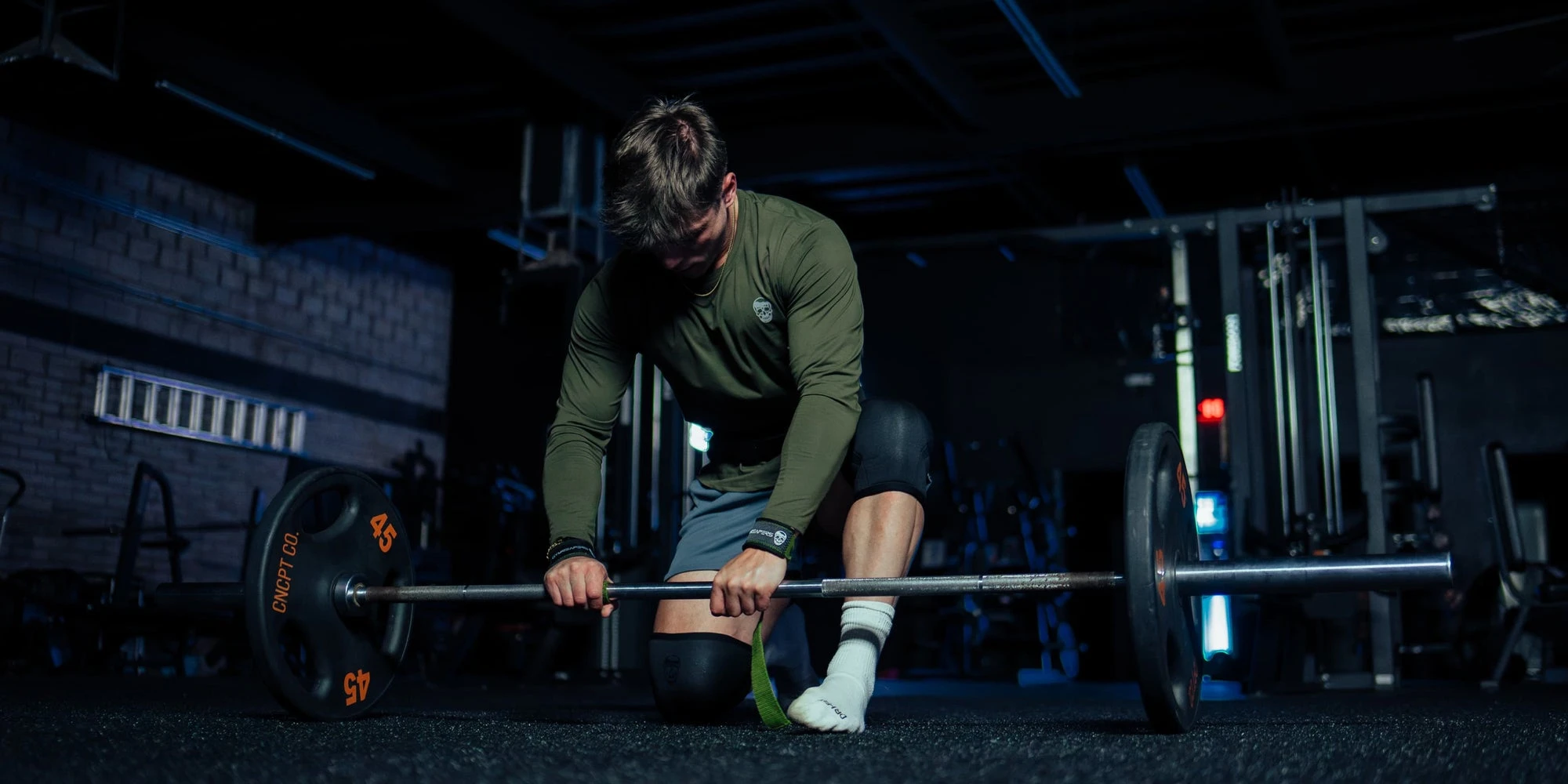 Athlete in an olive shirt setting up a deadlift in a dark gym